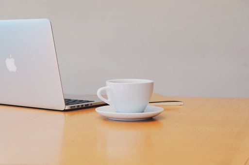 white coffee cup sits on a table next to a laptop